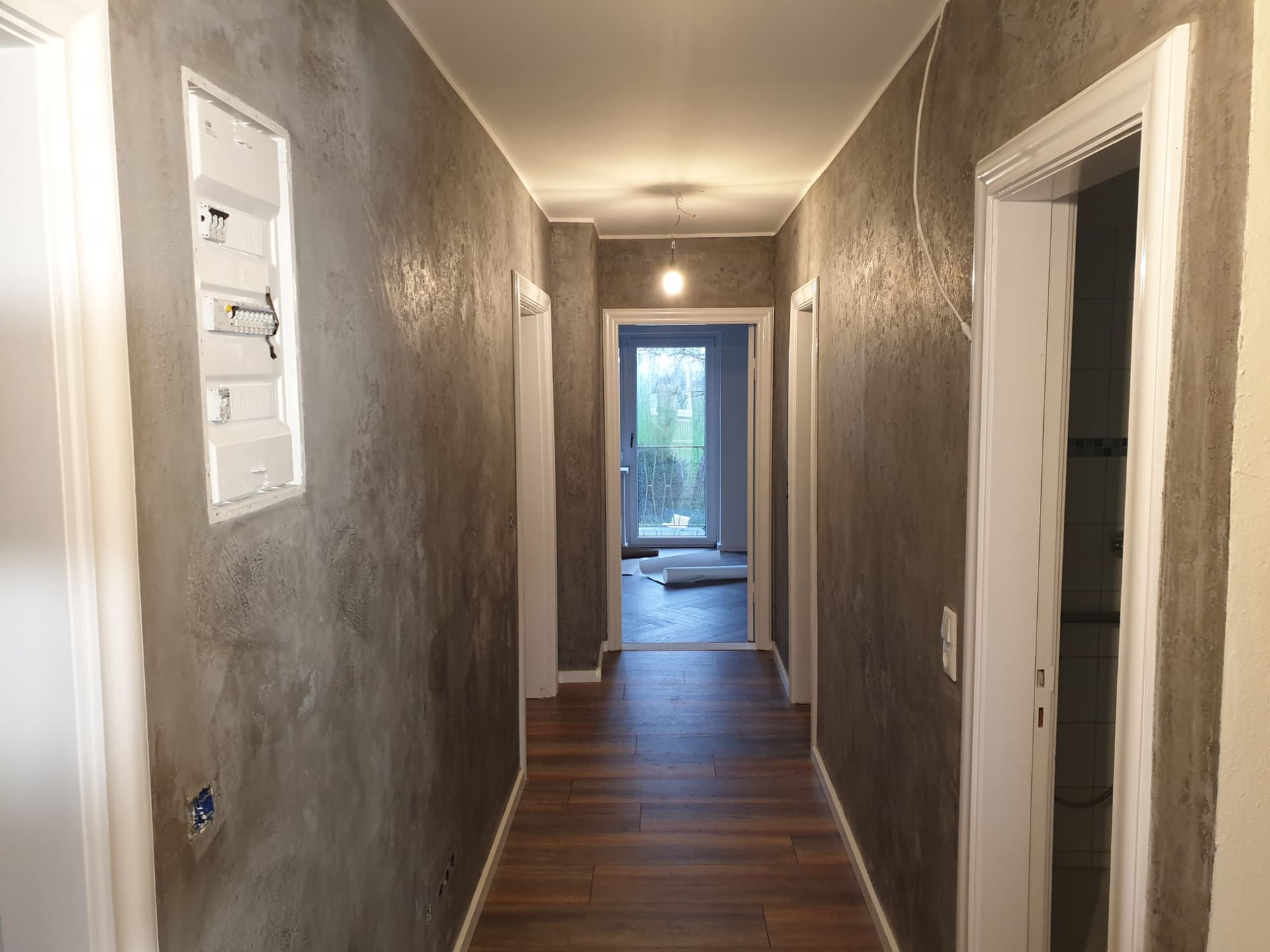 Flur mit Wänden in Betonoptik, am Ende eine Glastür