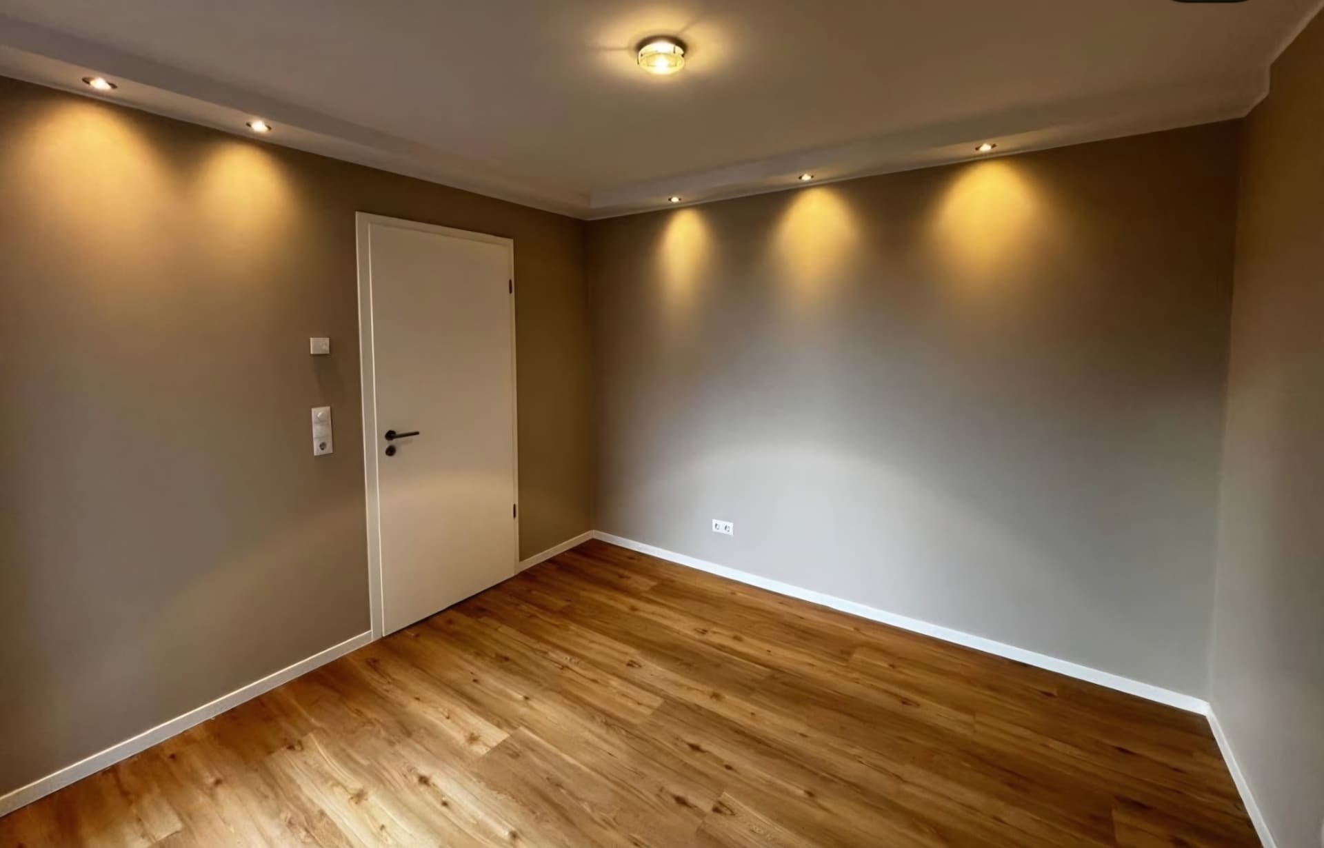 Leerer Raum mit warmgrauen Wänden, Deckenspots und Eichenboden